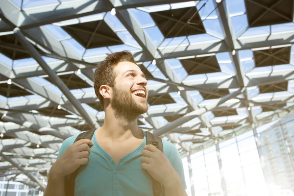 Veselý mladý muž s úsměvem s taškou na letišti — Stock fotografie