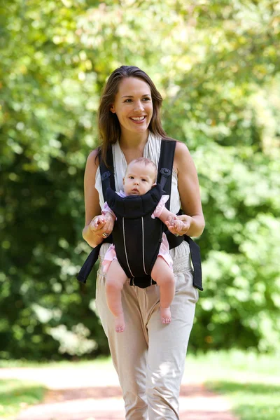 Sorrindo mãe andando ao ar livre com o bebê na funda — Fotografia de Stock