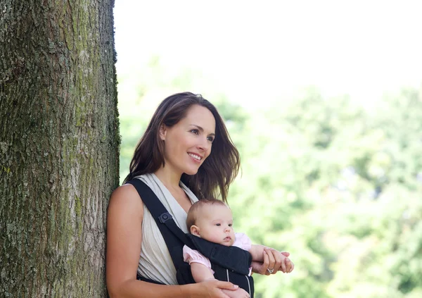 Mother smiling with infant in baby carrier — Stock Photo, Image