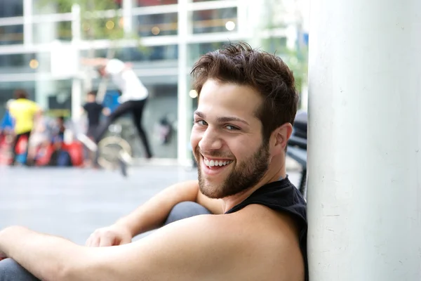Jovem sorridente com barba sentado do lado de fora — Fotografia de Stock
