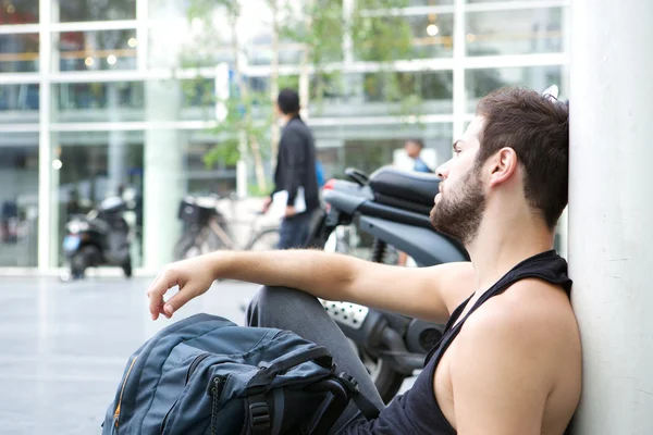 Jeune homme assis sur le sol dans la ville avec sac — Photo