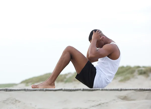 Młody człowiek wykonując na plaży robi siedzieć ups — Zdjęcie stockowe