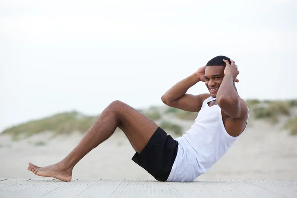 Zdrowy młody człowiek robi siedzieć ups na plaży — Zdjęcie stockowe