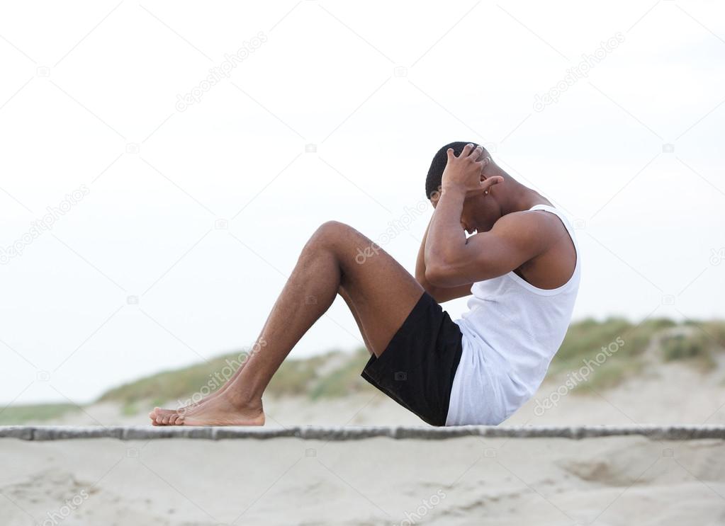 Young man exercising on the beach doing sit ups