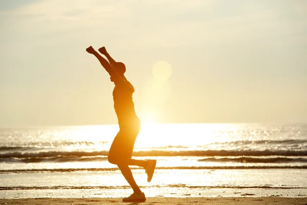 Un hombre corriendo por la playa con los brazos levantados — Foto de Stock