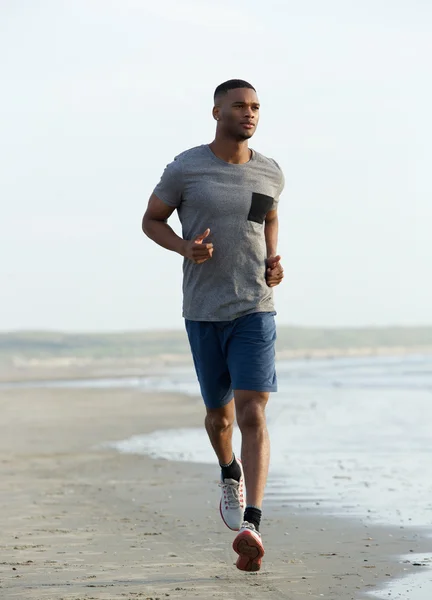 Junger schwarzer Mann läuft am Strand — Stockfoto