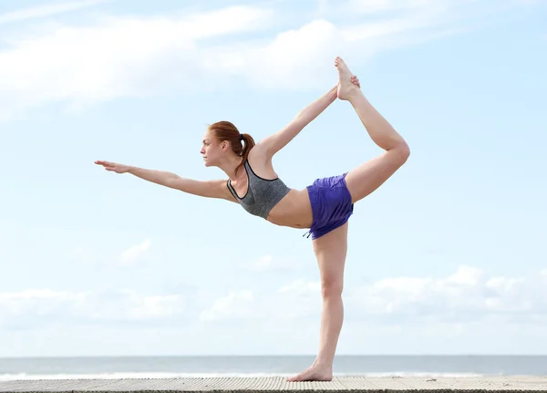 Mujer joven balanceándose sobre una pierna en posición de yoga — Foto de Stock