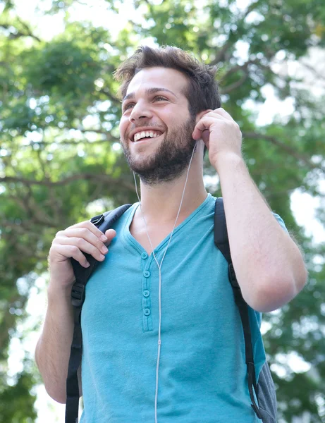 Giovane uomo sorridente con zaino e auricolari all'aperto — Foto Stock