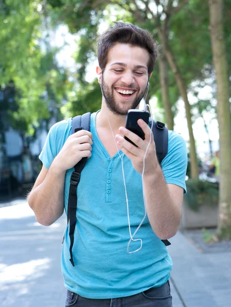 Młody człowiek uśmiechający się i patrząc na telefon komórkowy — Zdjęcie stockowe