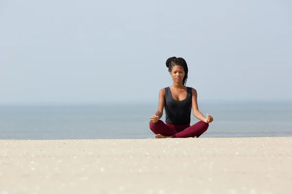 Afrikansk kvinna sitter vid stranden i yogaställning — Stockfoto