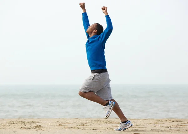 Man running at the beach with arms raised in victory — Stock Photo, Image