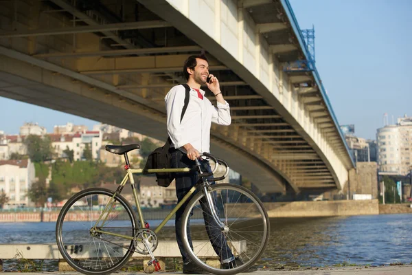 Bisiklet ile yürüyüş ve cep telefonu üzerinde konuşurken genç adam — Stok fotoğraf