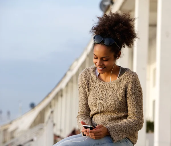 Mladá žena s úsměvem venku s mobilní telefon a sluchátka — Stock fotografie
