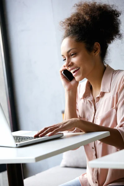Młoda kobieta rozmowa na telefon i patrząc na laptopa — Zdjęcie stockowe
