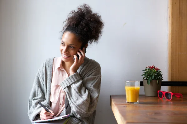 Junge Frau telefoniert mit Handy und macht sich Notizen — Stockfoto