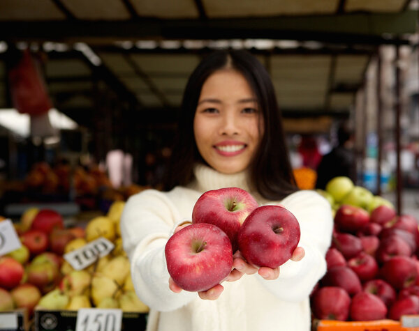 Молодая женщина улыбается красными яблоками в магазине
