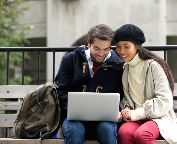 Glückliches junges Paar sitzt auf einer Bank und schaut auf Laptop — Stockfoto