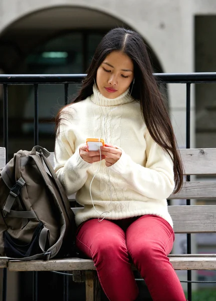 Mladá žena, sedící na lavičce v parku s mobilní telefon a sluchátka — Stock fotografie