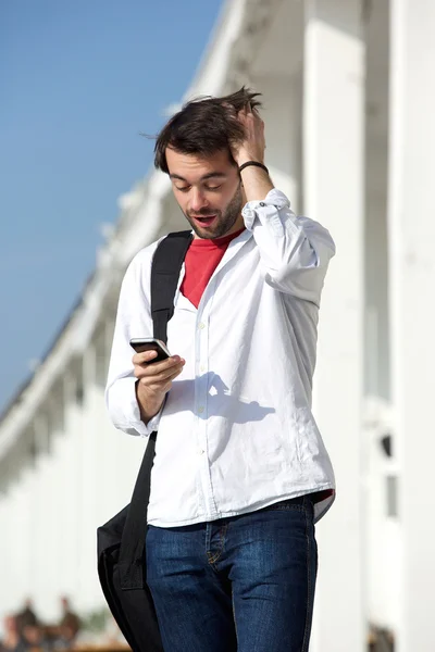 Mladý muž s překvapený výraz, při pohledu na mobilní telefon — Stock fotografie