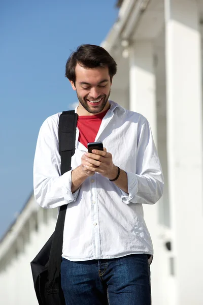 Mladý muž s úsměvem a při pohledu na mobilní telefon — Stock fotografie