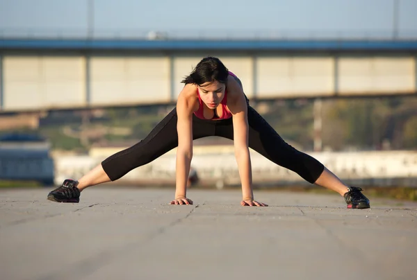 Giovane donna stiramento muscoli delle gambe con le mani sul pavimento — Foto Stock