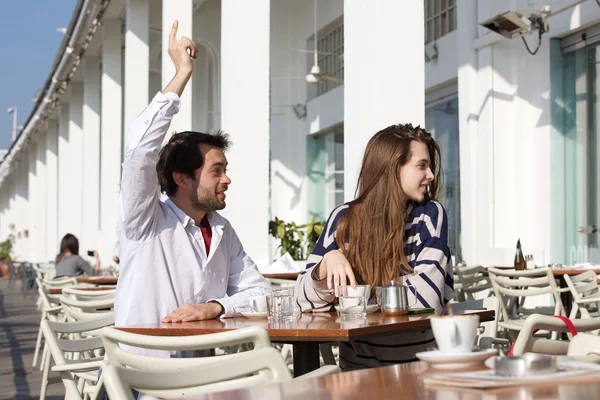 Joven sentado en la cafetería al aire libre con el brazo levantado pidiendo camarero —  Fotos de Stock