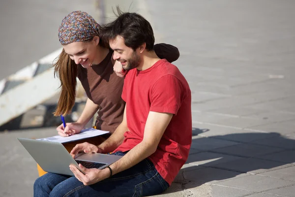 Samci a samice studenti sedí venku při pohledu na notebook — Stock fotografie