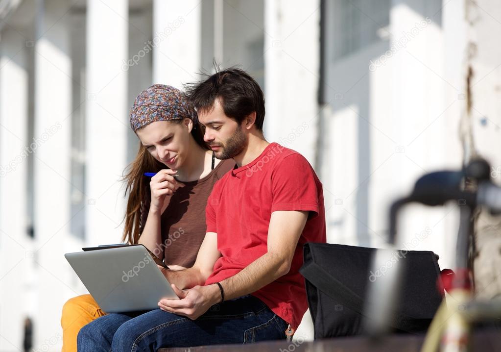 Two students sitting at campus looking at laptop together
