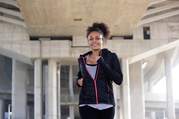 Lächelnde junge Frau joggt in urbaner Umgebung — Stockfoto