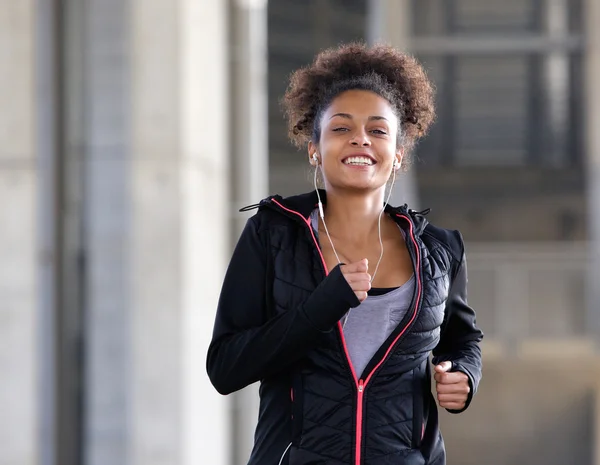 Lächelnde junge Frau läuft mit Kopfhörern ins Freie — Stockfoto