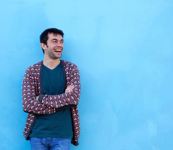 Jonge man die lacht met gekruiste op blauwe achtergrond armen — Stockfoto