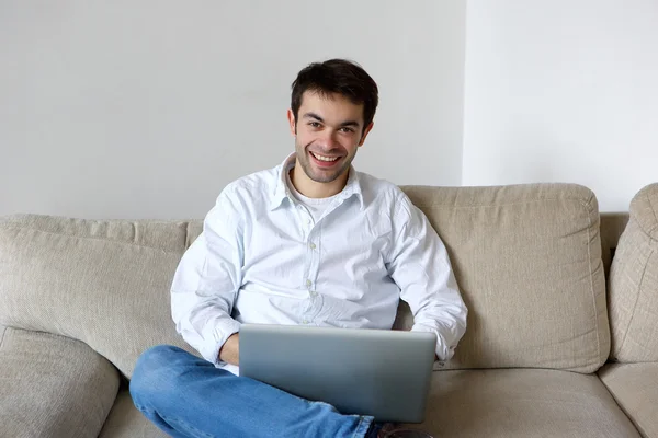 Jovem sorridente usando laptop em casa — Fotografia de Stock