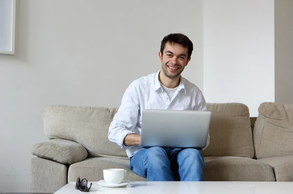 Młody człowiek uśmiechający się z laptopa w domu — Zdjęcie stockowe