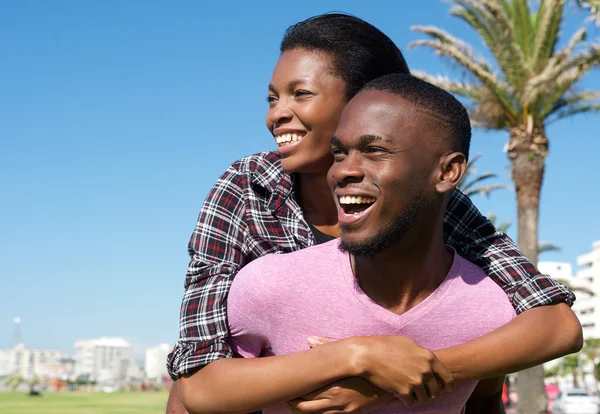 Happy young man carrying attractive girlfriend on his back — Stock Photo, Image