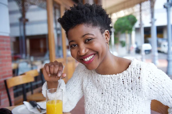 Jovem mulher negra atraente bebendo suco de laranja no restaurante — Fotografia de Stock