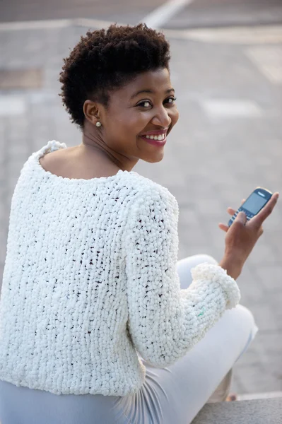 Unga afroamerikanska kvinnan leende med mobiltelefon — Stockfoto