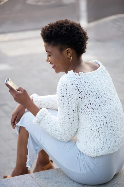 Mulher feliz sentada e enviando mensagem de texto no celular — Fotografia de Stock