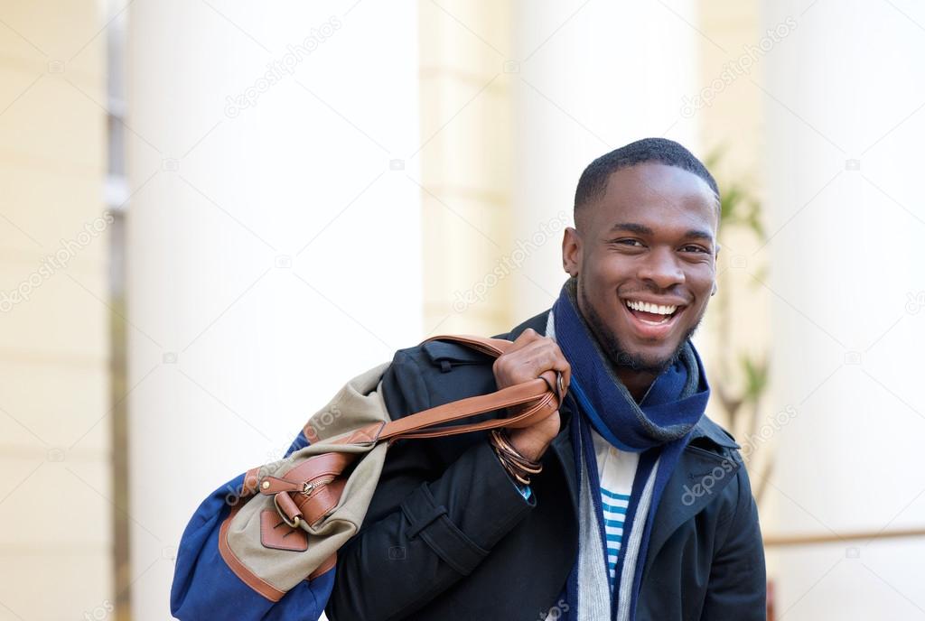 Happy traveling man standing outdoors with bag