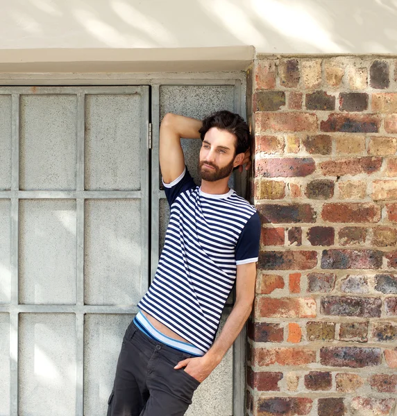 Young man with beard leaning against wall outdoors — Stock Photo, Image