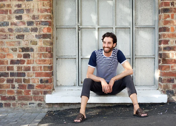 Happy young man with striped shirt sitting on windowsill — Stock Photo, Image