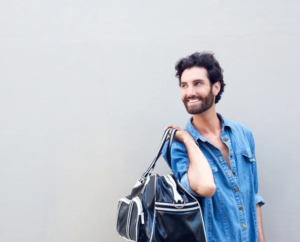 Uomo sorridente tenendo borsa da viaggio e guardando oltre la spalla — Foto Stock