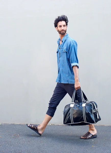 Side view portrait of a young man walking with travel bag