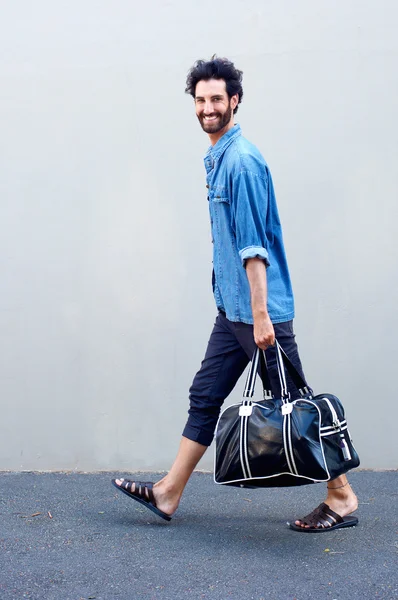 Homem moderno feliz andando e segurando saco de viagem — Fotografia de Stock