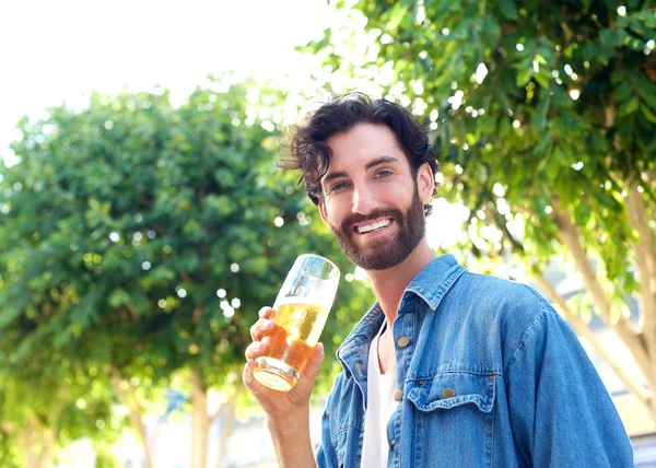 Knappe jonge man die lacht met een glas bier buiten — Stockfoto