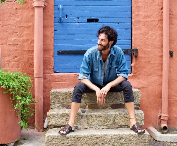 Coole modische junge Mann sitzt draußen auf Tür Schritt — Stockfoto