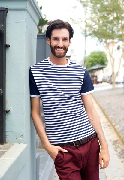 Happy trendy man in striped shirt leaning against wall outdoors — Stock Photo, Image