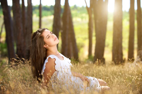 Drömmande ung kvinna sitter i fältet med solljus i bakgrunden — Stockfoto