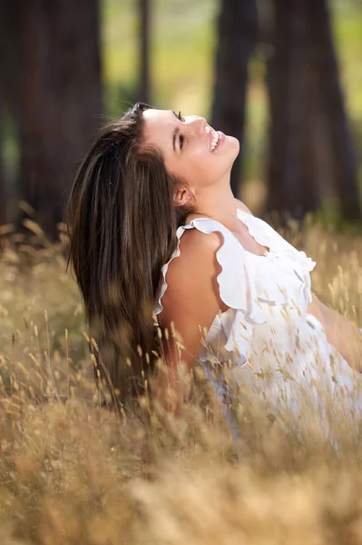 Happy young woman sitting in meadow and smiling — Stock Photo, Image