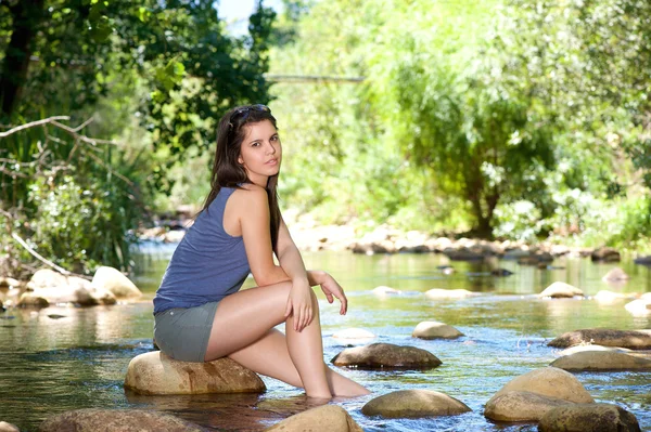 Woman sitting on rock by a stream with bare feet in water — Stock Photo, Image