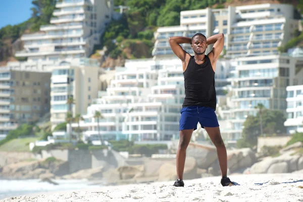 Schöner junger Sportler steht am Strand — Stockfoto
